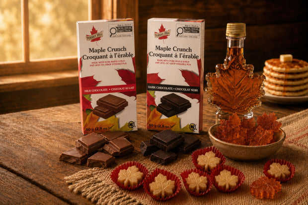 Canadian maple treats collection with Maple Crunch Belgian milk and dark chocolate bars, maple leaf syrup bottle, soft maple sugar candies, and amber maple candies on a rustic wooden table.