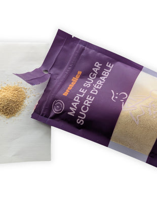 An opened 200 g pouch of fine maple sugar displayed beside a small pile of loose golden granules on a clean white background.  The angled package shows the bilingual label, transparent product window and torn opening while the loose sugar provides a clear view of its colour and texture.