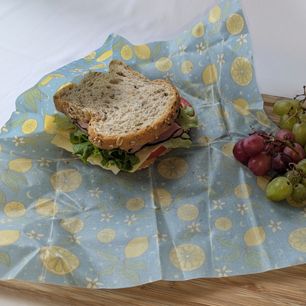 Lemon print beeswax wrap used as a reusable sandwich wrap with grapes on the side for a plastic-free lunch
