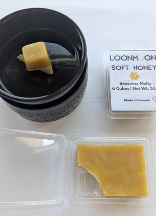 LOONMOON Soft Honey beeswax melts photographed with a black wax warmer, a single wax cube in the warmer dish, the closed clamshell package, and the open clamshell showing the wax inside.  This image gives customers a practical view of the product in use while also showing the packaging and natural beeswax appearance.