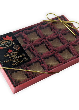 Angled view of a 15-piece soft maple sugar candy gift box made in Canada, showcasing individually wrapped maple leaf candies inside a premium red presentation box with decorative gold ribbon.  Authentic Canadian maple candy gift box made with pure maple syrup for gifting and special occasions.