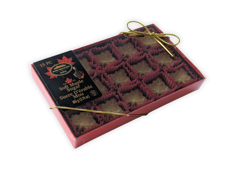 Angled view of a 15-piece soft maple sugar candy gift box made in Canada, showcasing individually wrapped maple leaf candies inside a premium red presentation box with decorative gold ribbon.  Authentic Canadian maple candy gift box made with pure maple syrup for gifting and special occasions.