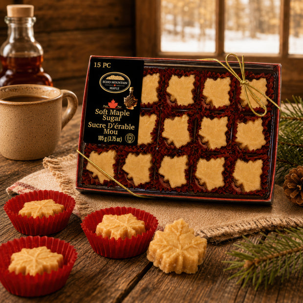 Soft maple sugar gift box with 15 organic Canadian maple candies on a rustic wooden table, styled with loose maple sugar pieces, a ceramic mug, syrup bottle, and evergreen branches in a cozy homestead setting.