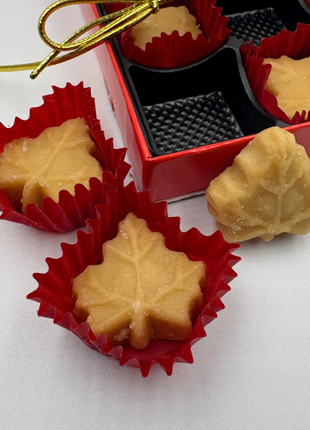 Close-up of soft maple sugar candies made from pure Canadian maple syrup, shaped like maple leaves in red paper cups, with a gift box in the background