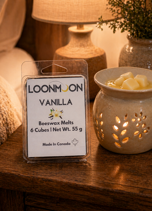 LOONMOON Vanilla beeswax wax melts beside a glowing ceramic warmer on a cozy rustic bedside table.
